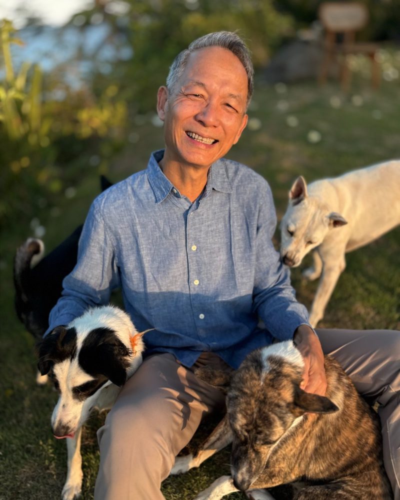 Leng Lim seated on the grass in evening light, with four dogs around him